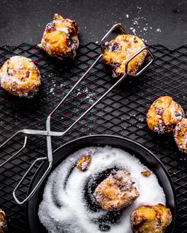 Ein schwarzer Tisch mit kleinen Gebäckbällchen und einer Zuckerschale.