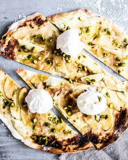 Flammkuchen aufgeschnitten mit Äpfeln belegt und mit Vanilleeis und Pistazien bestreut.