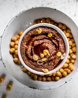 Schokoladen-Hummus mit ganzen Kichererbsen in einer Schale, von oben fotografiert auf hellem Untergrund.