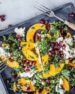 Bunter Salat mit Grünkohl, Kürbis und Granatapfel auf eckigem dunklen Teller