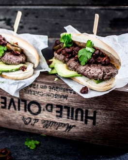 Burger mit länglichem Hackfleischpatty, schwarzen Bohnen und Avocado.