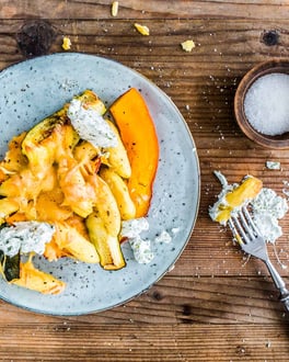 Schupfnudeln mit Kürbis und Zucchini überbacken mit Käse auf einem grau-blauen Teller auf Holzuntergrund.