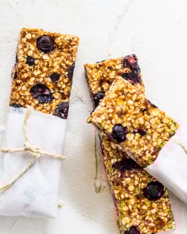 Müsliriegel mit Blaubeeren in Backpapier verpackt auf weißem Tisch.