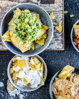 Nachos in vier Schälchen mit vier verschiedenen Saucen auf dunklem Untergrund