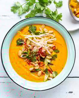 Süßkartoffel-Suppe mit Topping aus Sprossen, Frühlingszwiebeln, Chili, Erdnüssen und Koriander auf weißem Tisch