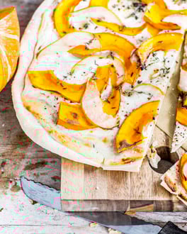 Angeschnittener Flammkuchen mit Kürbisspalten und Kräutern auf Holzuntergrund