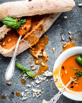 Tomatensuppe im Brotlaib, daneben eine Schüssel mit Tomatensuppe mit Basilikum dekoriert.