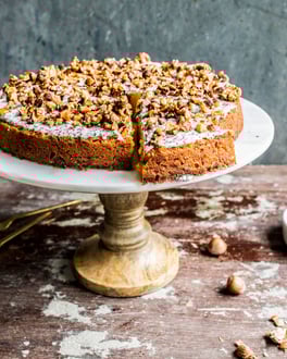 Runder Kürbiskuchen getoppt mit Mohn-Schmand und Haselnussstücken auf Tortenplatte mit Holzfuss