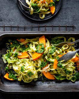 Dunkle graue Auflaufform mit Tagliatelle, Pesto und Kürbisspalten.