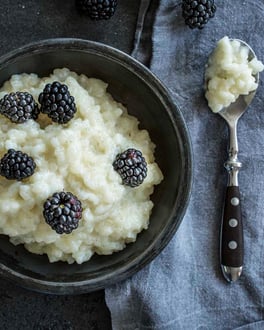 Milchreis in dunkler Schale angerichtet mit Brombeeren auf dunklem Untergrund