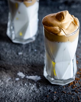 Zwei Gläser mit Milch und Dalgona Coffee auf schwarzem Tisch.