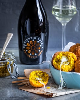 Mit Käse und Pesto gefüllte Arancini in blauer Schale mit Prosecco im Hintergrund