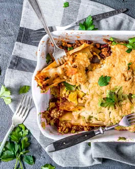 Rechteckige weiße Auflaufform mit überbackenen Chili con Carne-Canneloni und Petersilie auf grauem Tuch