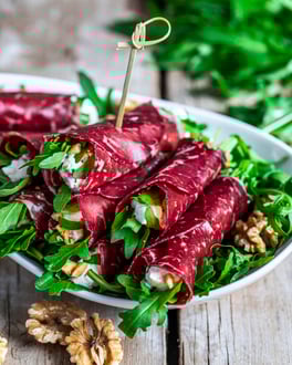 Bresaola-Rouladen auf einem Rucola-Bett mit Walnusskernen auf einem weißen Teller