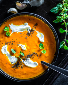 Kürbissuppe mit Schmand und Mohn-Topping in einer schwarzen Schüssel