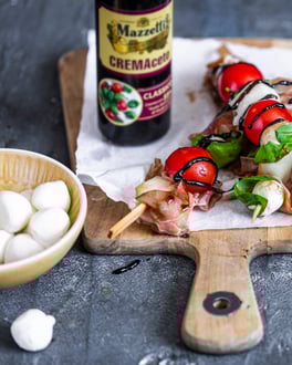 Melonenspieße mit Parmaschinken, Tomaten und Mozzarella auf einem Holzbrett mit Balsamicocreme verziert