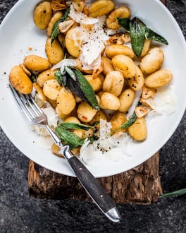 Einfache Salbei-Gnocchi mit gehobeltem Parmesan auf einem weißen Teller mit Gabel.