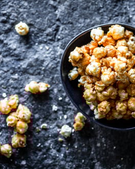 Salted Caramel Popcorn in einer dunklen Schale auf dunklem Grund, von oben fotografiert. Etwas Popcorn liegt neben der Schale.