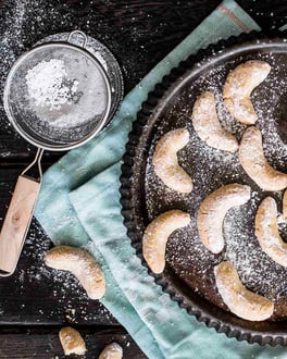 Vanillekipferl mit Puderzucker auf einer Tarteform serviert und einer mintfarbener Stoffserviette.