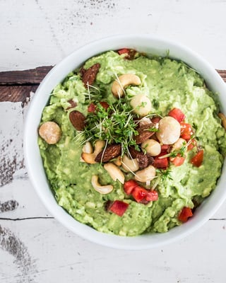 Guacamole, getoppt mit Nüssen, Tomate und Kresse in einer weißen Schale.