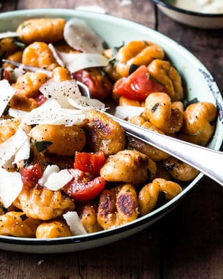 Süßkartoffel-Gnocchi mit Tomaten und Parmesan und in einem Teller mit Löffel.