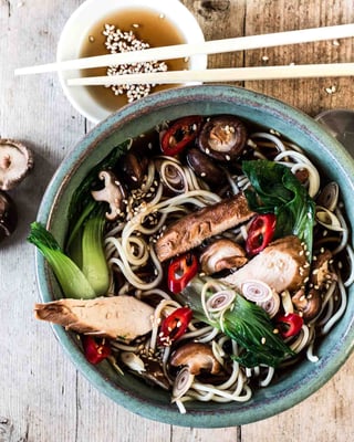 Asiatische Nudelsuppe mit Hähnchen von oben fotografiert mit Essstäbchen und chinesischem Suppenlöffel auf Holzuntergrund