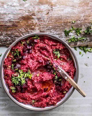 Selbst gemachter Hummus mit Rote Bete auf rustikalem Untergrund mit Petersilie garniert, ein Holzlöffel steckt im Dip.