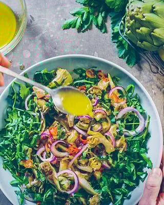 Artischockensalat wird mit Dressing beträufelt
