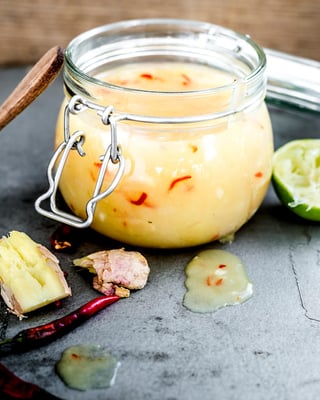 gelbe Chilisauce in Weckglas auf hellem Beton mit Limette und Kochlöffel