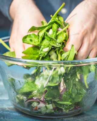 Blattspinat wird in einer Schüssel von Hand als Salat gemischt.