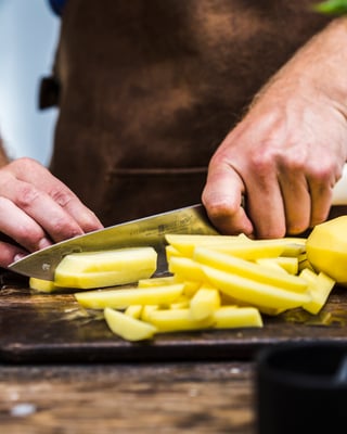 Hände, die Kartoffeln auf Holzbrett zu Pommes schneiden
