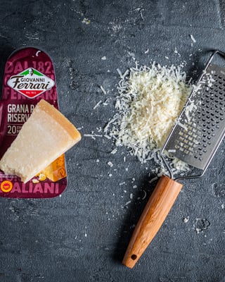 Grana Padano, geriebener Käse, Parmesanchip auf dunklem Untergrund