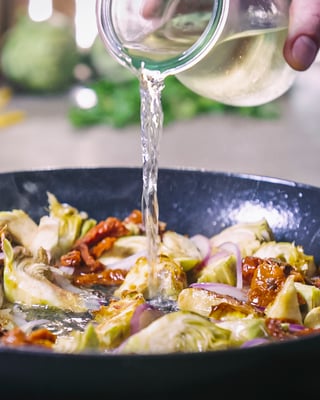 Penne mit Artischocken werden mit Weißwein abgelöscht