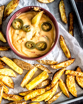 Selbstgemachte Pommes auf silbernem Blech mit Chili-Cheese-Dip in Schale