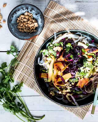 Glasnudelsalat mit Pak Choi in einer Schale mit Essstäbchen auf einer Bambusmatte neben einer Schale mit Nüssen