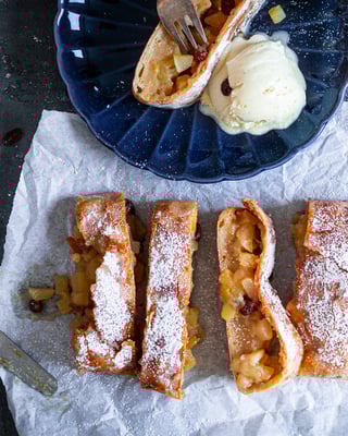 Italienischer Apfelstrudel auf Backpapier mit Vanilleeis und Puderzucker