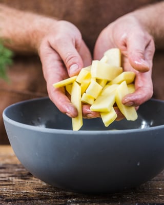 Hände legen Kartoffelsticks in eine Schale mit kaltem Wasser