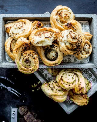 Knoblauchteigschnecken mit Thymian in eckigen Schälchen mit kleinen Gäbelchen auf schwarzem Untergrund.