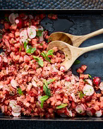 Schwarzes Backblech mit rotem Wassermelonen-Radieschen-Salat und Holzlöffeln.