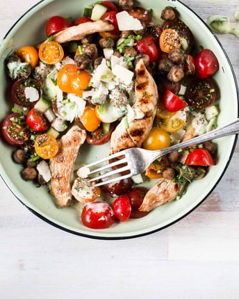 Tomaten-Kichererbsen-Salat mit würzigen Hähnchenstreifen auf hellem Untergrund