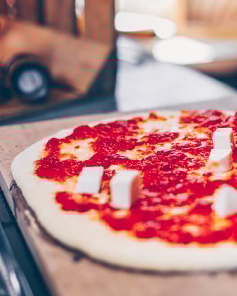 Pizza Margherita wird von Hand mit Mozzarellastückchen belegt