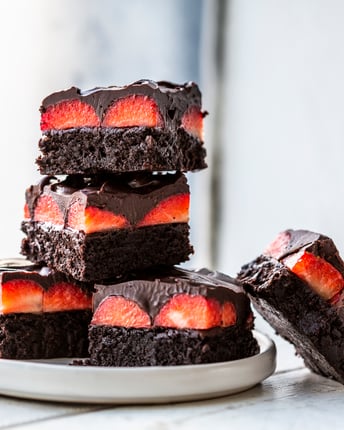 Erdbeer-Brownies mit Schoko-Ganache, gestapelt auf einem Teller vor dem Fenster.