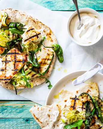 Gegrillter Halloumi in Fladenbrot mit Paprika, Zucchini, Frisée und Rucola auf türkisem Holztisch.