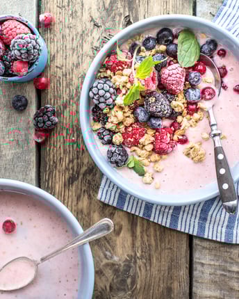 Zwei Schalen mit rosa Smoothie Bowl getoppt mit gefrorenen Beeren und Müsli auf Holztisch