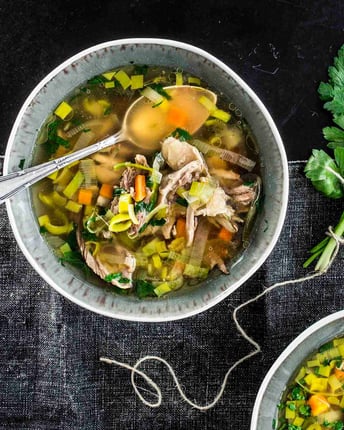 Hühnersuppe mit Gemüse in kleinen Suppenschälchen mit Löffel.