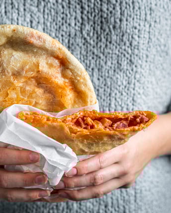 Frittierte Pizza wird vor grauem Strickpulli in den Händen gehalten