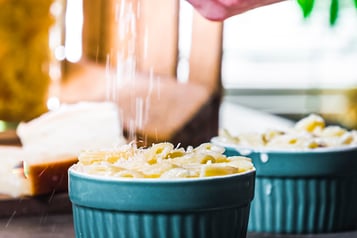 Mini-Nudelauflauf in türkisenen Förmchen. die mit Käse bestreut werden
