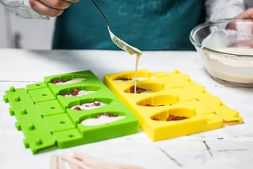 Auf eine Schicht Kompott in den Stieleisförmchen folgt eine Schicht Joghurt, die mit einem Löffel hineingegeben wird.