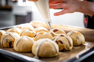 Die Hot Cross Buns werden mit einem weißen Kreuz aus der Spritztülle dekoriert.