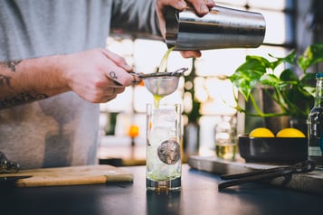 Die Rucola-Limonade wird mit Hilfe eines Strainers in ein Longdrinkglas gefüllt.